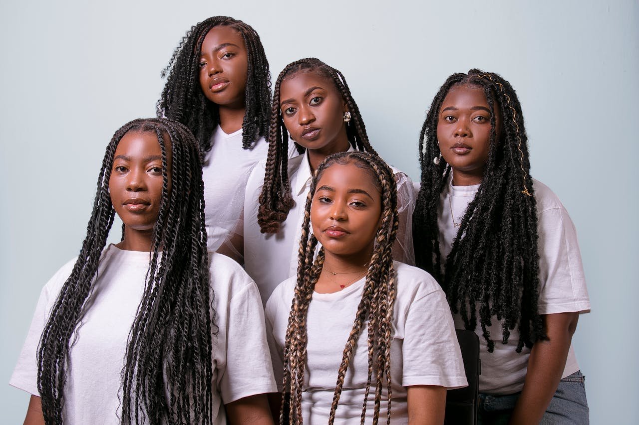 A stylish group portrait of five women showcasing braided hairstyles in white shirts.