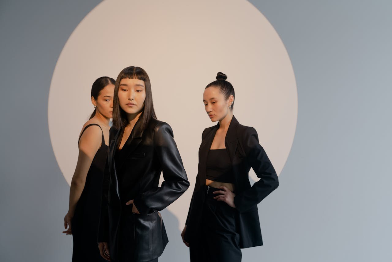 Fashionable studio shoot of three women posing in black outfits under a spotlight.